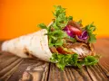 Kebab zawinięty w placek z mięsem, warzywami i sałatą na drewnianym stole.