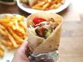 Domowy kebab z kurczakiem, warzywami i frytkami, trzymany w ręce.