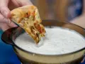 Kawałek pizzy zanurzany w białym sosie czosnkowym z ziołami.