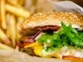 Soczysty burger wołowy z serem, warzywami i frytkami w papierowym opakowaniu.