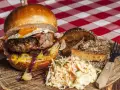 Burger z jajkiem sadzonym, boczkiem, frytkami i surówką colesław na drewnianej desce.