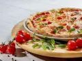 Pizza z pomidorkami koktajlowymi i ziołami na drewnianej desce.