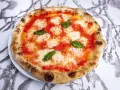Pizza Margherita z pomidorami, mozzarellą i bazylią na białym talerzu na marmurowym tle.