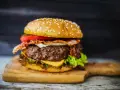 Soczysty hamburger z bekonem, serem, pomidorem i sałatą na desce.