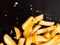 Złociste frytki posypane solą na czarnym tle.