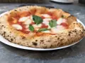Pizza Margherita na białym talerzu, z widocznym puszystym brzegiem i świeżą bazylią.
