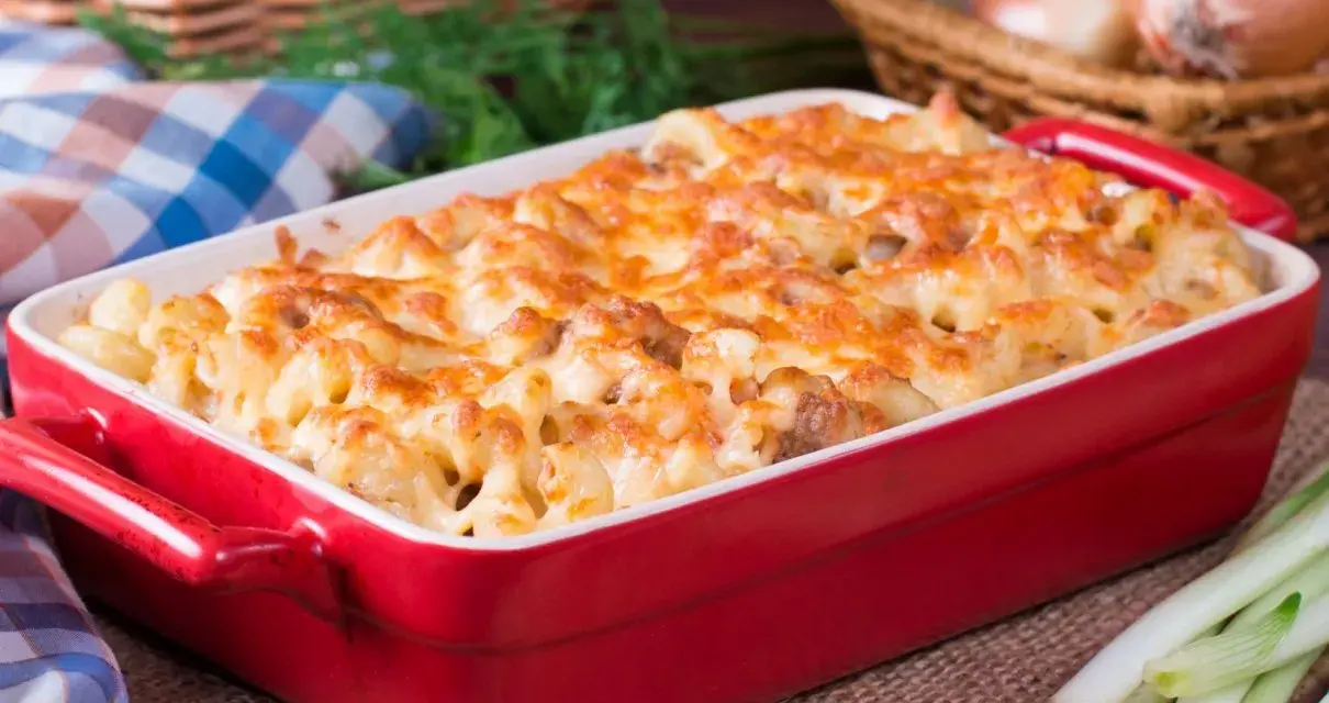 Zapiekanka makaronowa z kurczakiem w czerwonym naczyniu, posypana roztopionym serem.