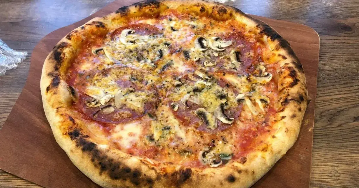 Domowa pizza z pieczarkami i salami na drewnianej desce.