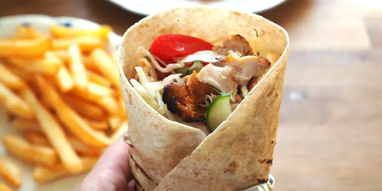 Domowy kebab z kurczakiem, warzywami i frytkami, trzymany w ręce.
