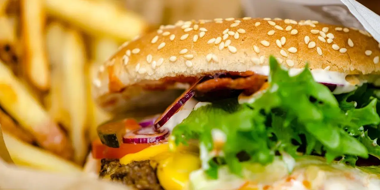 Soczysty burger wołowy z serem, warzywami i frytkami w papierowym opakowaniu.