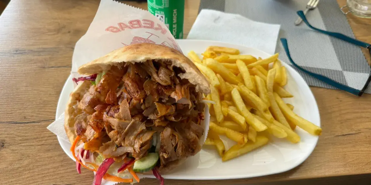 Kebab z frytkami na talerzu, obok puszka napoju.