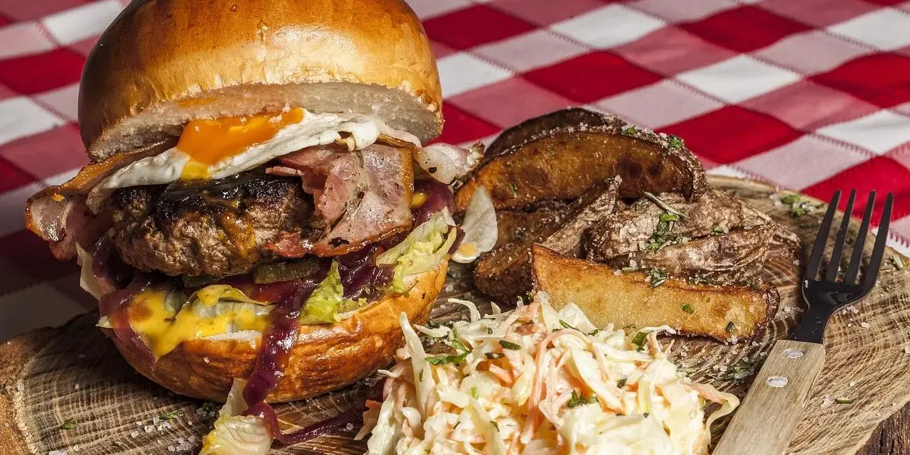 Burger z jajkiem sadzonym, boczkiem, frytkami i surówką colesław na drewnianej desce.