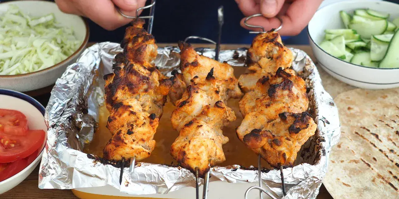 Domowy kebab: grillowane szaszłyki z kurczaka w tacce, obok miseczki z warzywami i tortille.