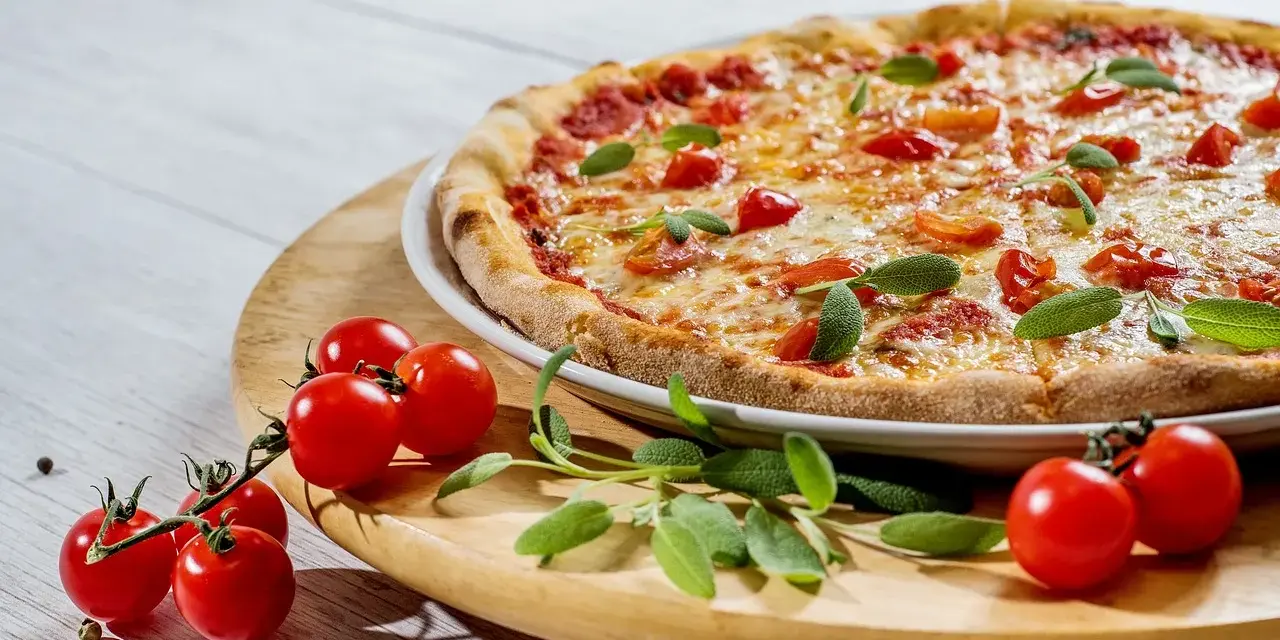 Pizza z pomidorkami koktajlowymi i ziołami na drewnianej desce.