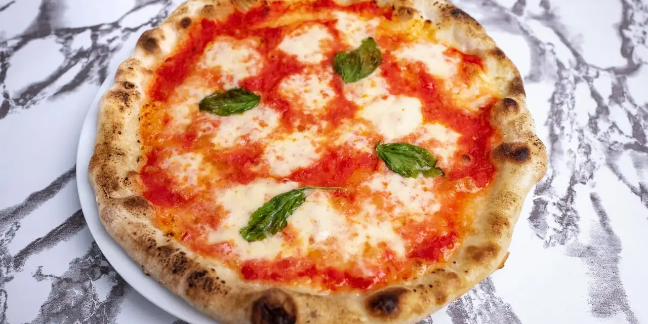 Pizza Margherita z pomidorami, mozzarellą i bazylią na białym talerzu na marmurowym tle.