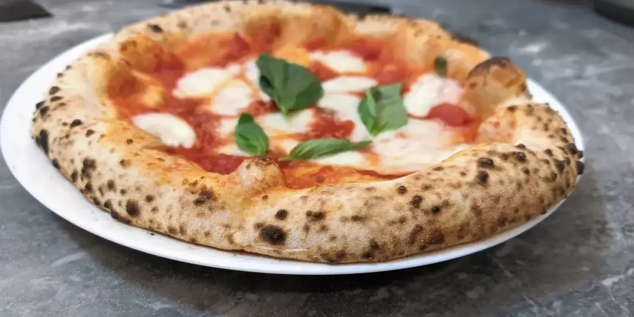 Pizza Margherita na białym talerzu, z widocznym puszystym brzegiem i świeżą bazylią.