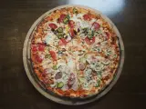Duża, okrągła pizza z różnymi dodatkami: salami, pieczarkami, korniszonami i papryczkami jalapeno.