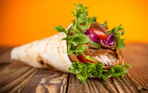 Kebab zawinięty w placek z mięsem, warzywami i sałatą na drewnianym stole.