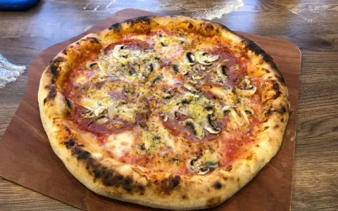 Domowa pizza z pieczarkami i salami na drewnianej desce.