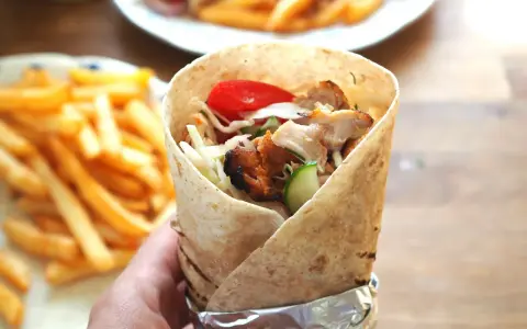Domowy kebab z kurczakiem, warzywami i frytkami, trzymany w ręce.