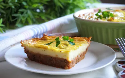 Wegańska zapiekanka pasterska z ziemniaczanym puree i warzywnym farszem, udekorowana natką pietruszki.