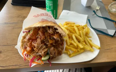 Kebab z frytkami na talerzu, obok puszka napoju.
