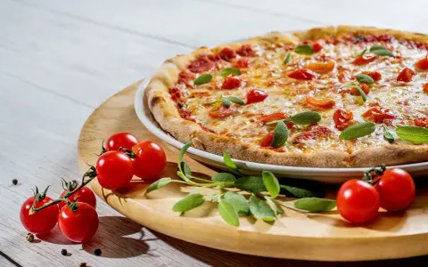 Pizza z pomidorkami koktajlowymi i ziołami na drewnianej desce.