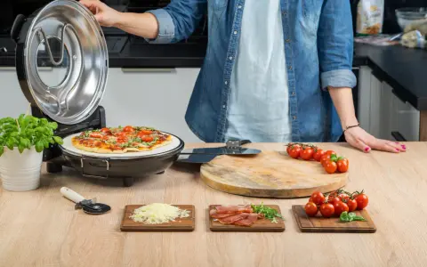Gotowa pizza w piecyku, składniki na blacie: pomidorki, ser, rukola, szynka.
