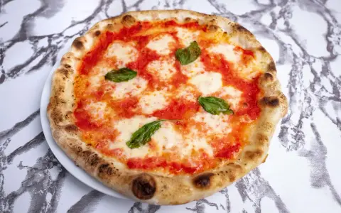 Pizza Margherita z pomidorami, mozzarellą i bazylią na białym talerzu na marmurowym tle.