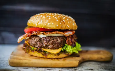 Soczysty hamburger z bekonem, serem, pomidorem i sałatą na desce.