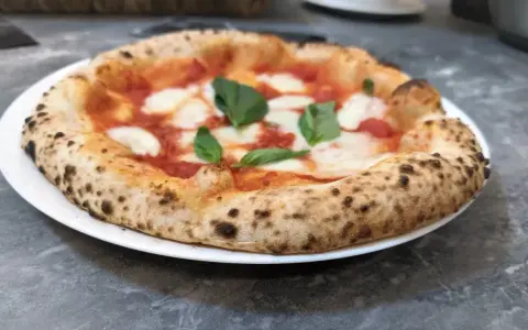 Pizza Margherita na białym talerzu, z widocznym puszystym brzegiem i świeżą bazylią.