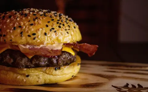 Soczysty domowy burger z bekonem i serem na bułce z sezamem.