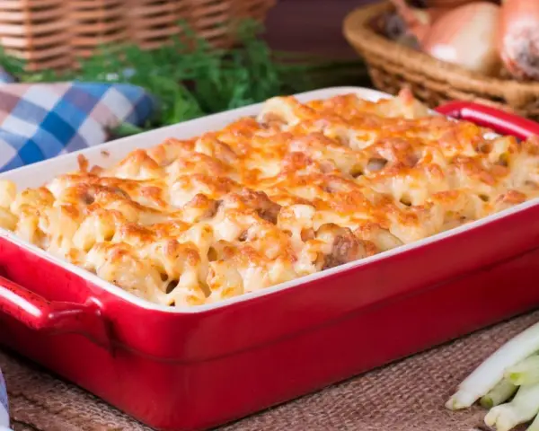 Zapiekanka makaronowa z kurczakiem w czerwonym naczyniu, posypana roztopionym serem.