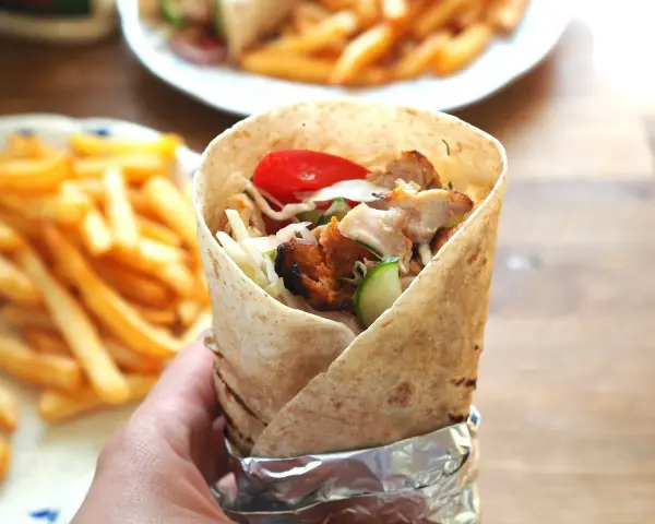 Domowy kebab z kurczakiem, warzywami i frytkami, trzymany w ręce.