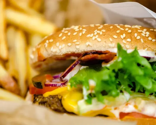 Soczysty burger wołowy z serem, warzywami i frytkami w papierowym opakowaniu.