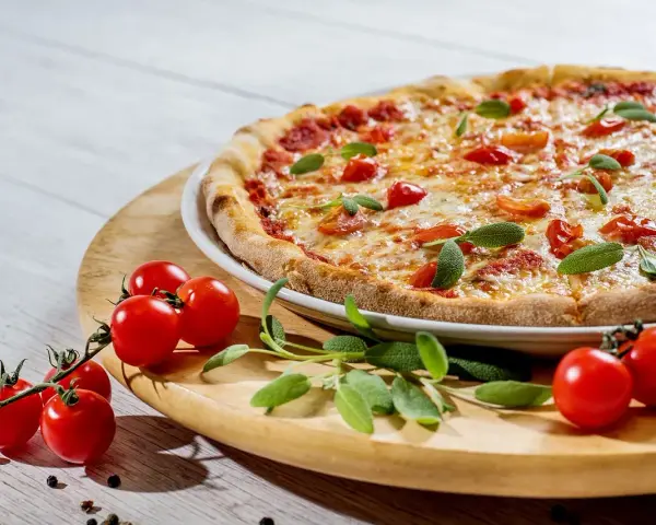 Pizza z pomidorkami koktajlowymi i ziołami na drewnianej desce.