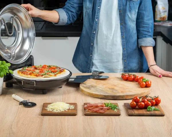 Gotowa pizza w piecyku, składniki na blacie: pomidorki, ser, rukola, szynka.