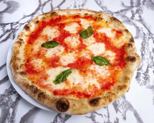 Pizza Margherita z pomidorami, mozzarellą i bazylią na białym talerzu na marmurowym tle.