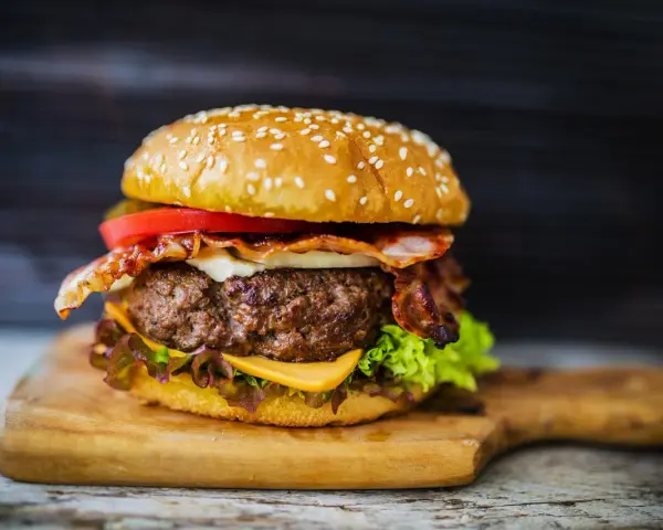 Soczysty hamburger z bekonem, serem, pomidorem i sałatą na desce.
