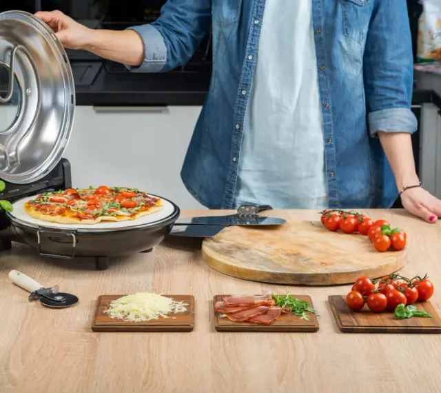 Gotowa pizza w piecyku, składniki na blacie: pomidorki, ser, rukola, szynka.