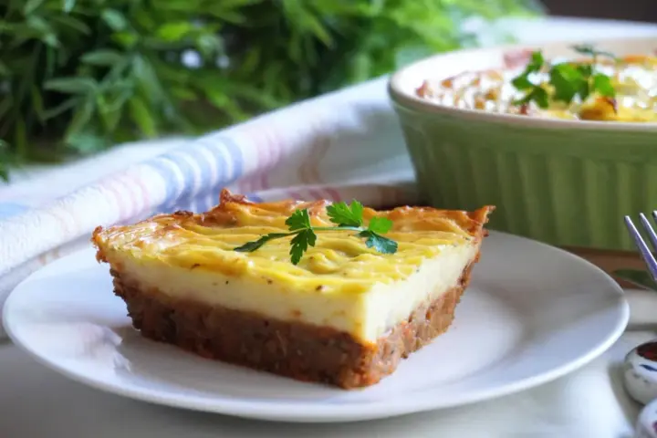 Wegańska zapiekanka pasterska z ziemniaczanym puree i warzywnym farszem, udekorowana natką pietruszki.