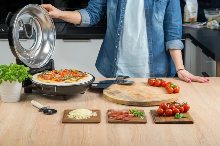 Gotowa pizza w piecyku, składniki na blacie: pomidorki, ser, rukola, szynka.