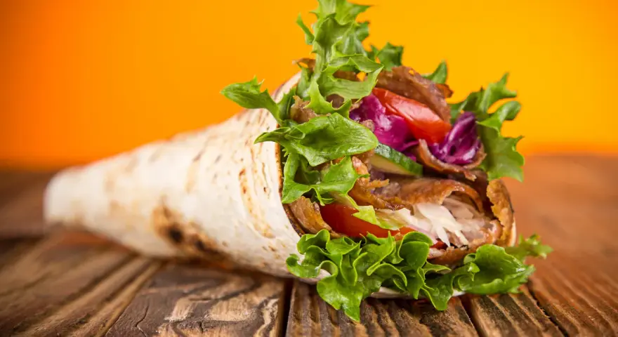 Kebab zawinięty w placek z mięsem, warzywami i sałatą na drewnianym stole.