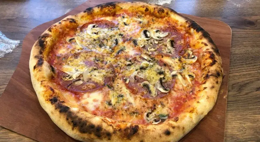 Domowa pizza z pieczarkami i salami na drewnianej desce.