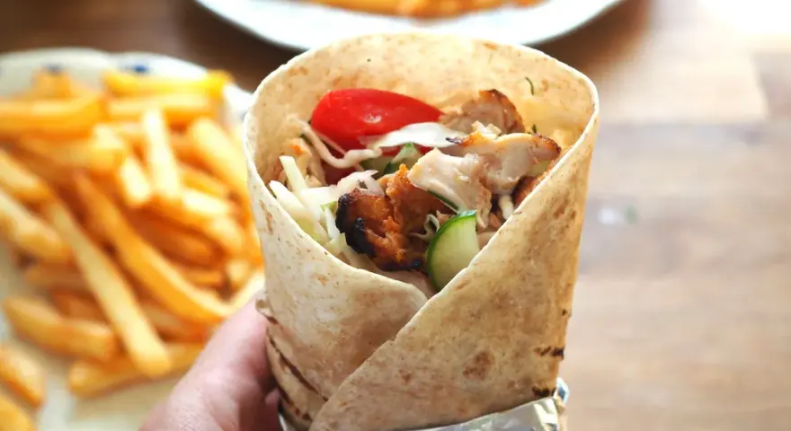 Domowy kebab z kurczakiem, warzywami i frytkami, trzymany w ręce.