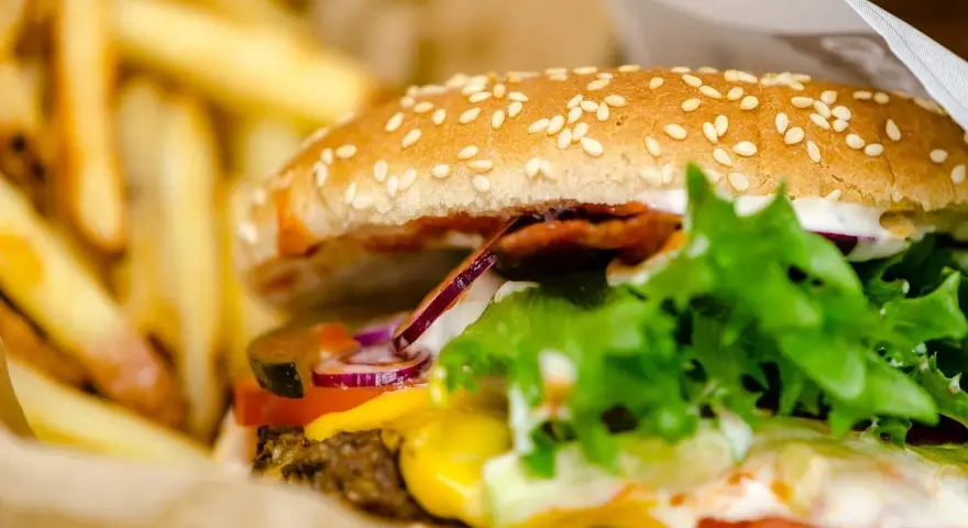 Soczysty burger wołowy z serem, warzywami i frytkami w papierowym opakowaniu.