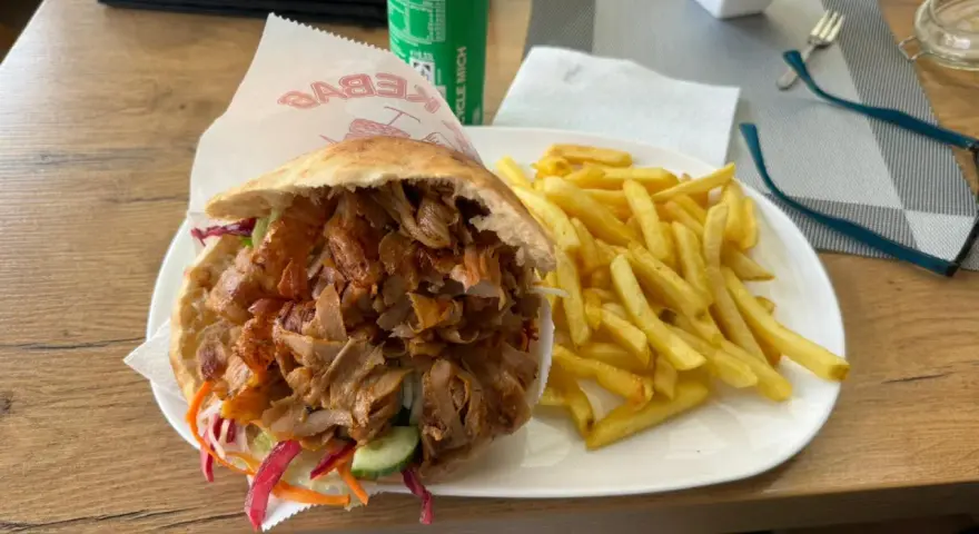 Kebab z frytkami na talerzu, obok puszka napoju.