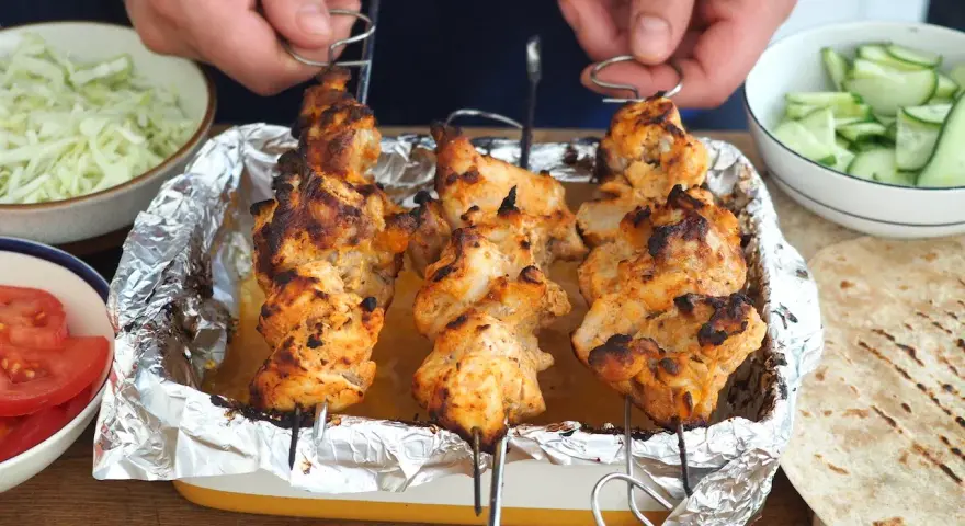 Domowy kebab: grillowane szaszłyki z kurczaka w tacce, obok miseczki z warzywami i tortille.