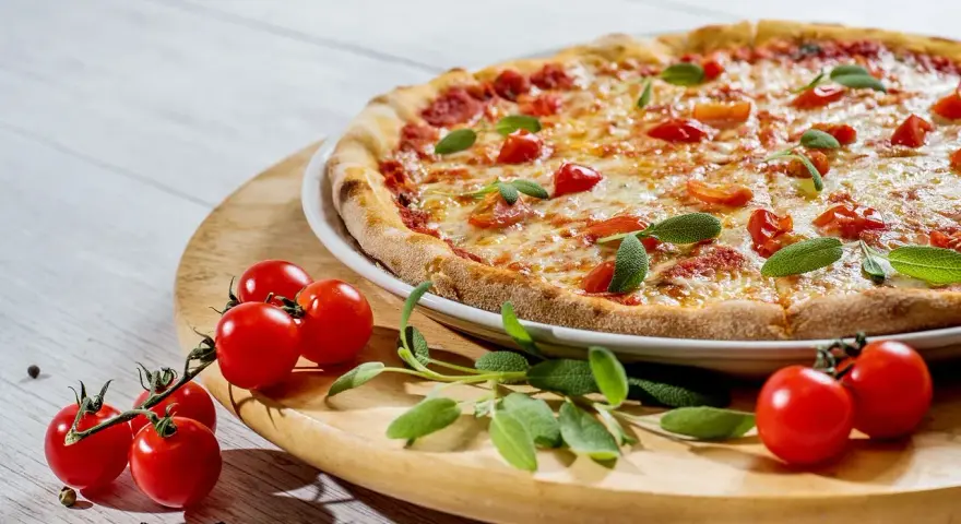 Pizza z pomidorkami koktajlowymi i ziołami na drewnianej desce.