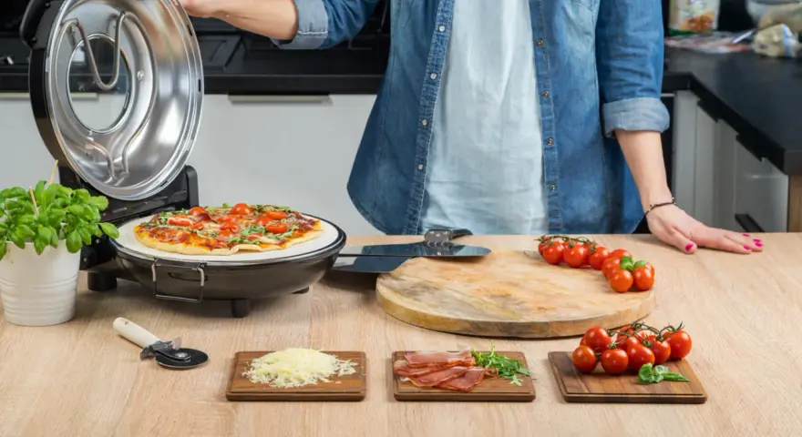Gotowa pizza w piecyku, składniki na blacie: pomidorki, ser, rukola, szynka.